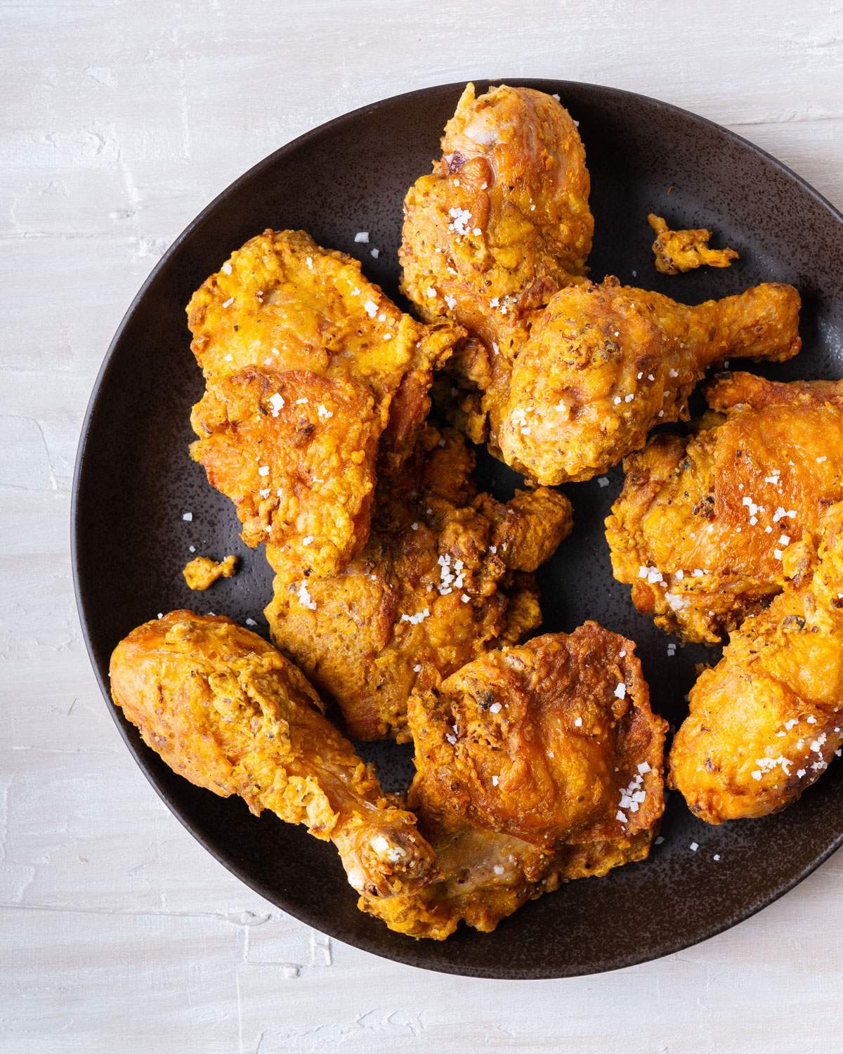 Crispy fried chicken pieces with flaky sea salt on a dark plate