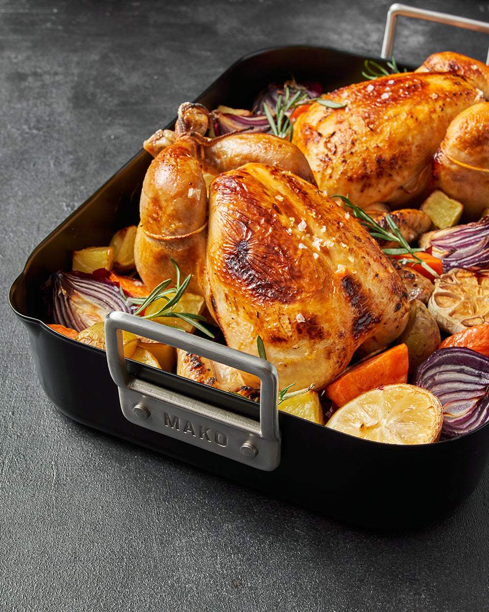 Golden roasted chicken with potatoes, carrots, onions, and lemon in a black roasting pan