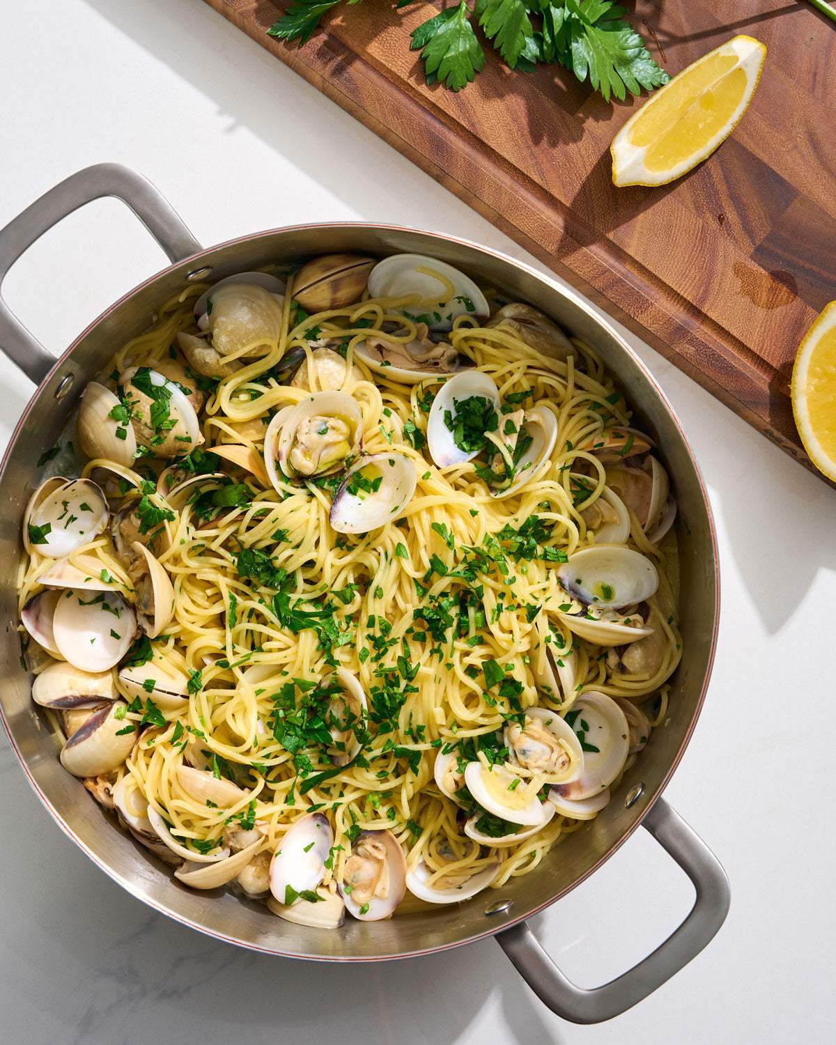 Cookware with spaghetti alle vongole, fresh parsley, and lemon on cutting board