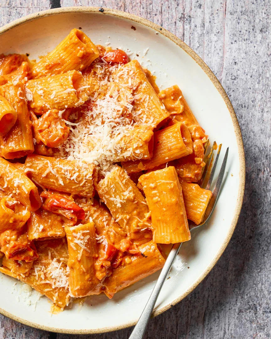 Creamy red rigatoni pasta with cherry tomatoes and grated cheese on white plate with fork