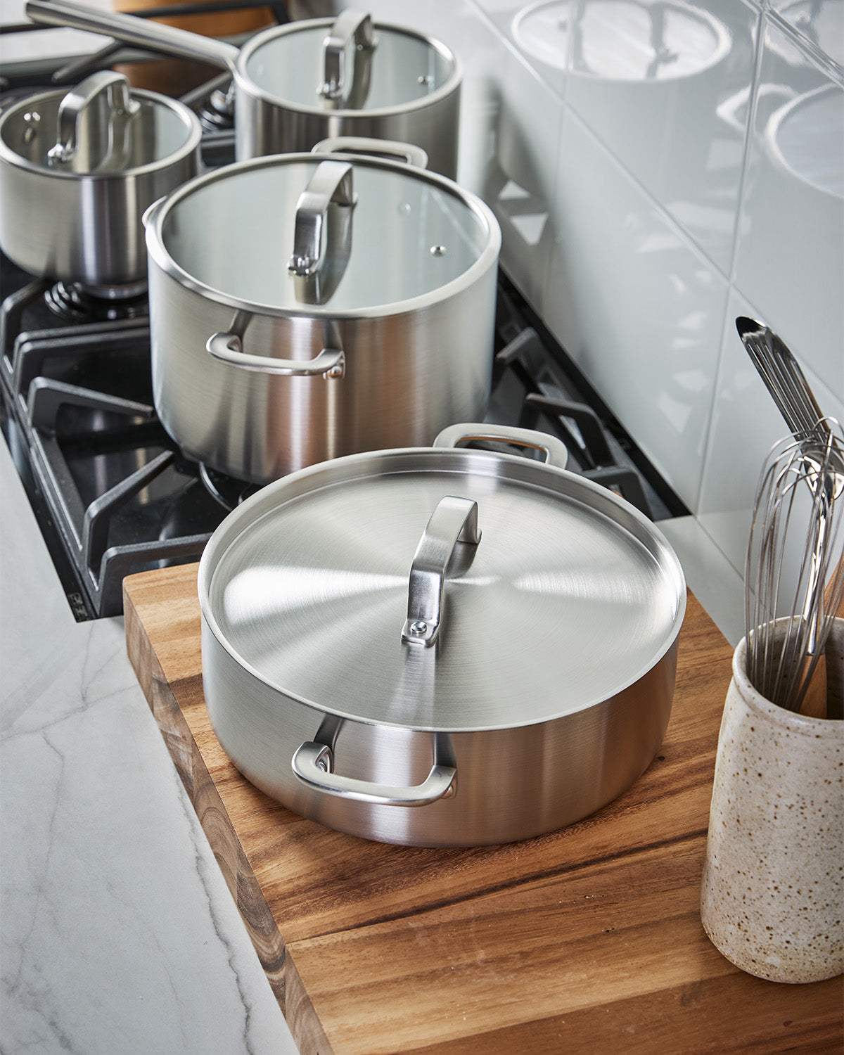 Stainless steel cookware set with glass lids on a modern stovetop and wooden countertop