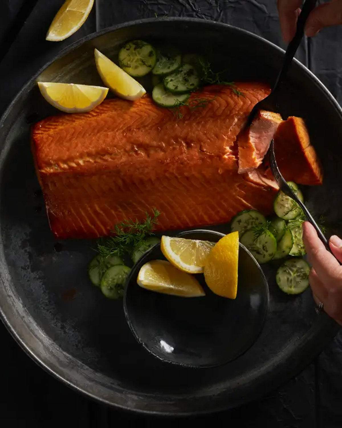 Smoked salmon fillet on a plate with fresh cucumber slices and lemon wedges
