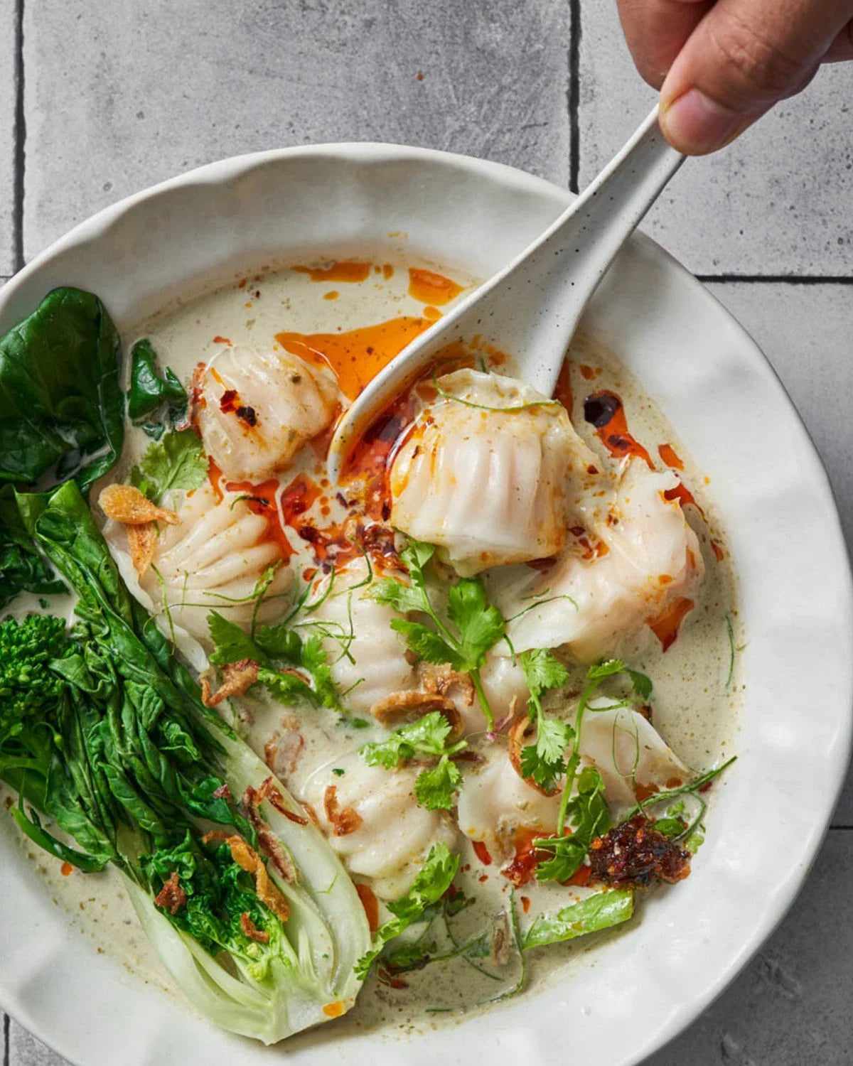 Thai green curry dumpling soup with bok choy, chili oil, and fresh cilantro in a white bowl