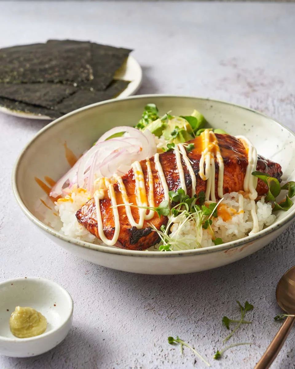 Spicy salmon sushi bowl with rice, avocado, microgreens, and mayonnaise drizzle, served with nori.