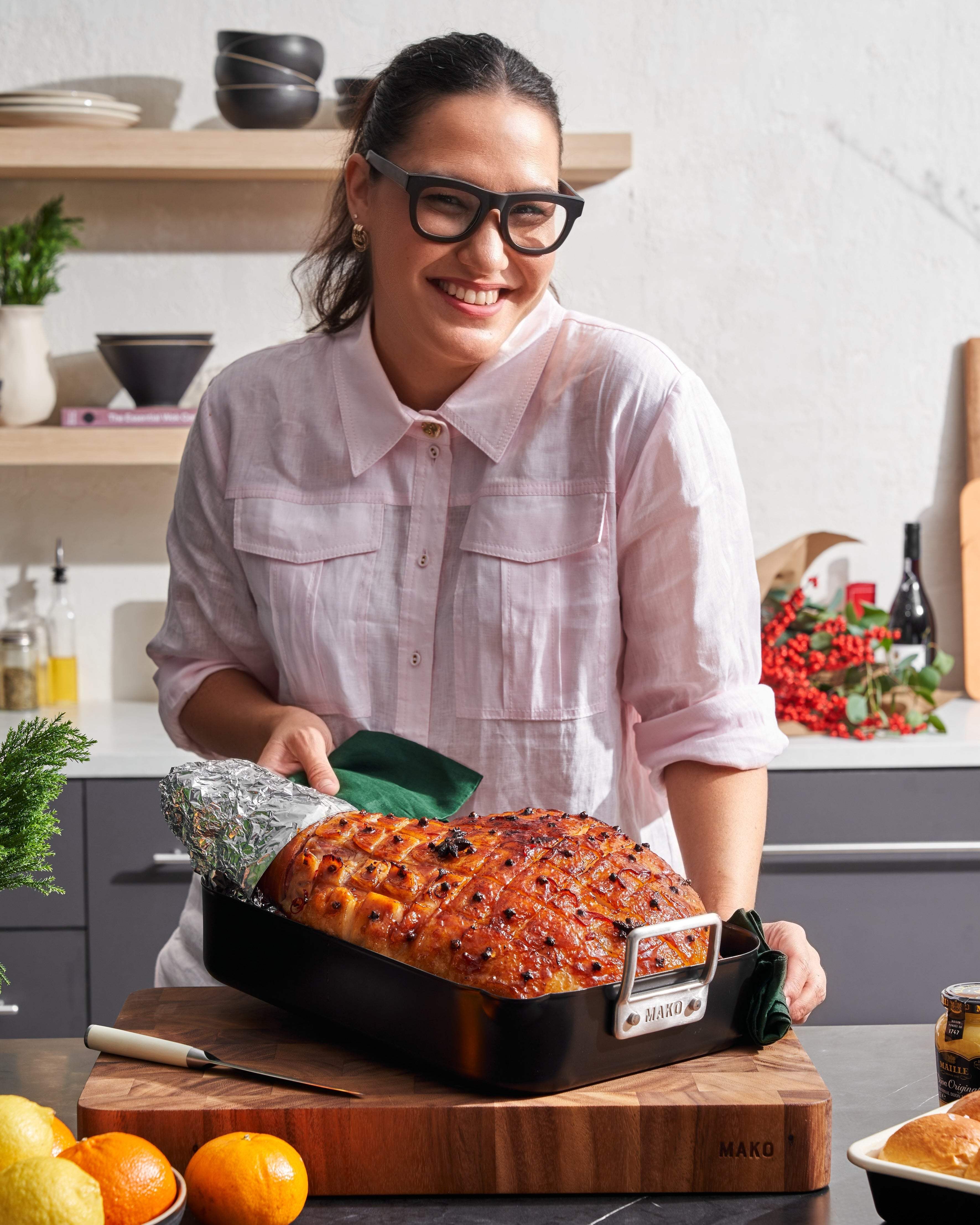 Smiling woman in glasses holding a glazed Christmas ham in a Mako roasting pan in a modern kitchen