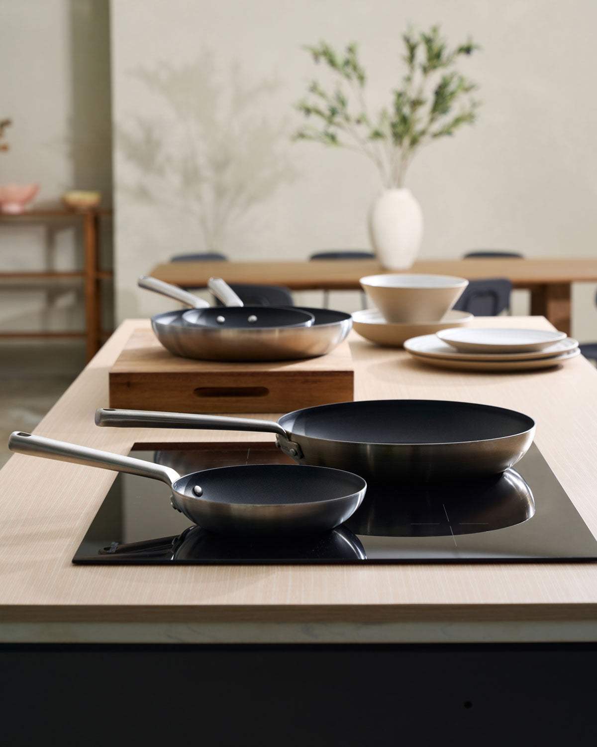 Modern kitchen with stainless steel nonstick frying pans, ceramic plates and bowls on a wooden island.