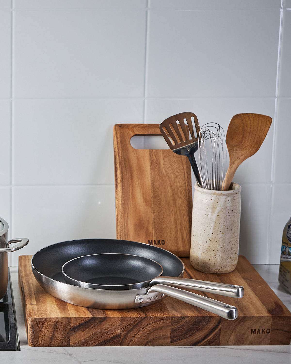 Non-stick frying pans on wooden chopping board with utensils in kitchen setting