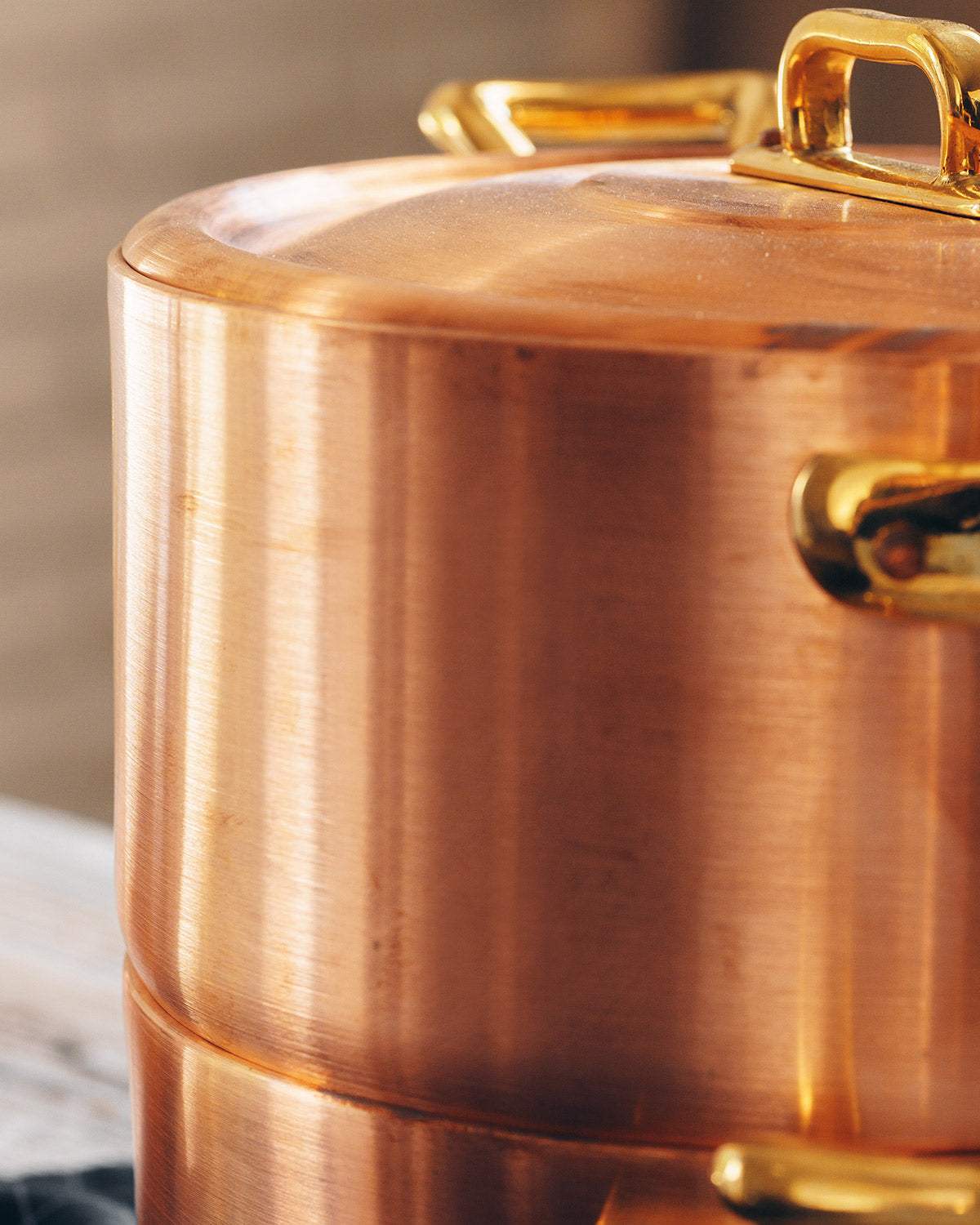 Close-up of stacked copper cookware pots with gold handles on a kitchen surface