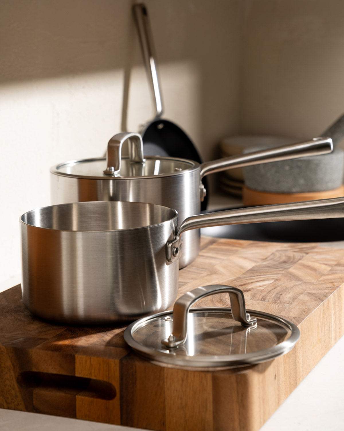 Stainless steel saucepan set with lids on a wooden cutting board in a modern kitchen