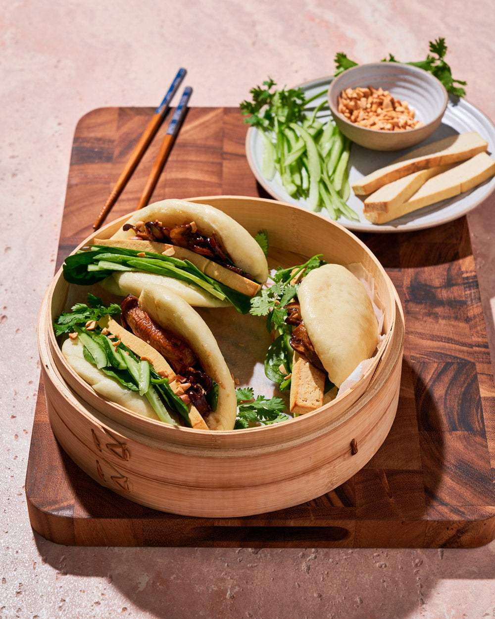 Steamed bao buns filled with smoked tofu, cucumber, greens, and herbs on a wooden board