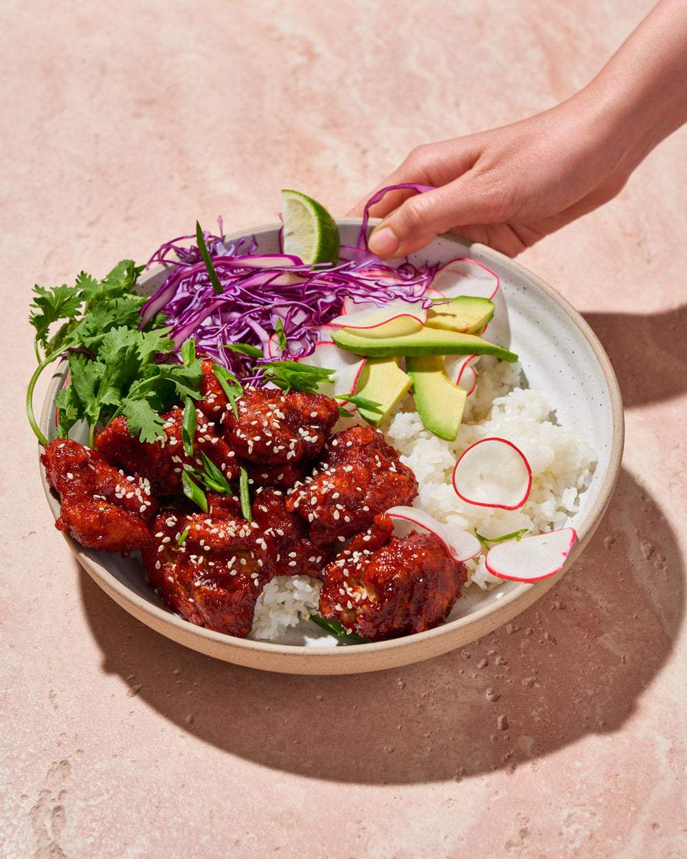 Korean fried chicken bowl with rice, avocado, radish, lime, purple cabbage, cilantro