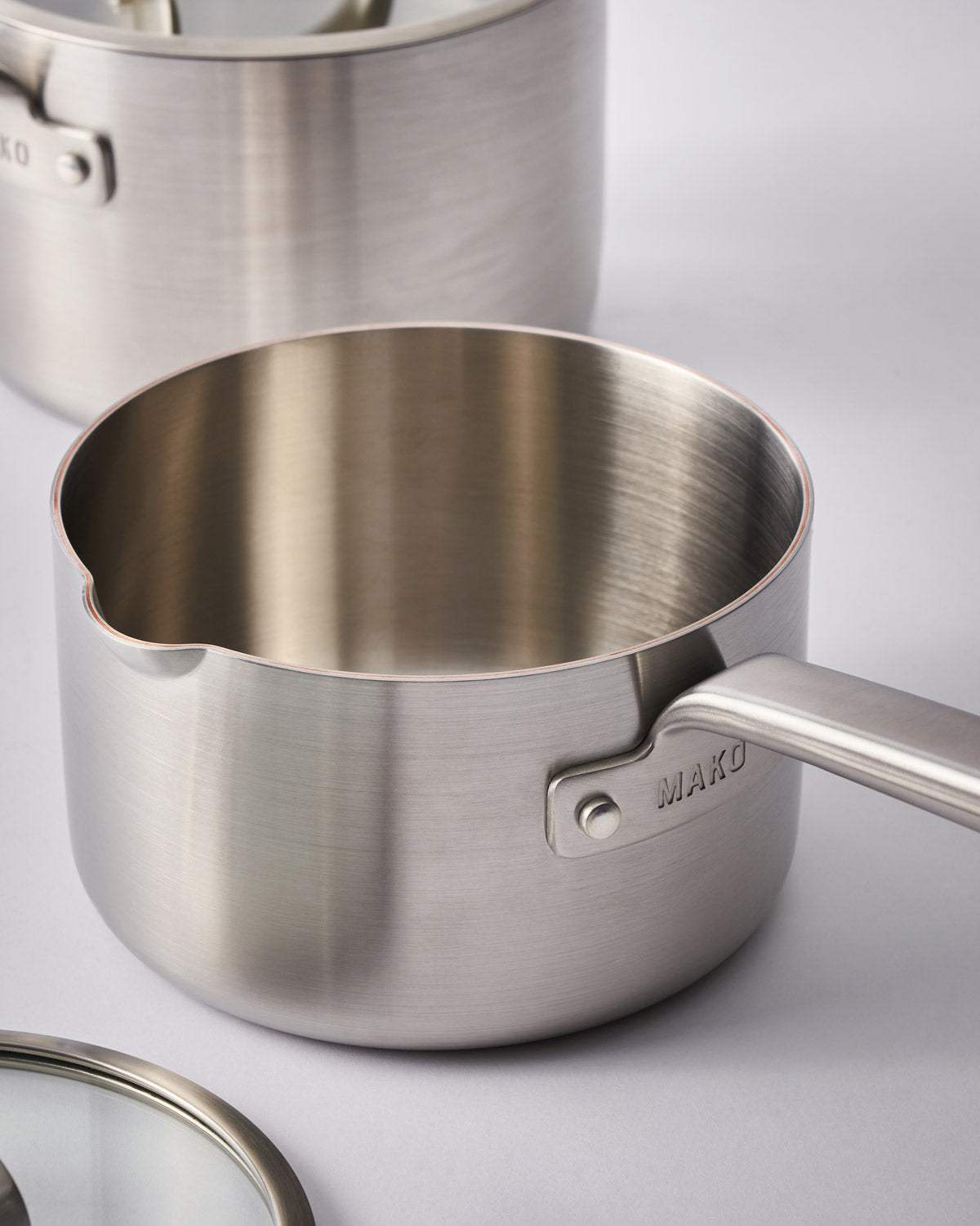 Stainless steel saucepan with long handle and pouring spout on a light background