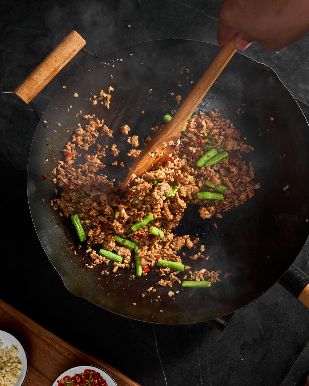 Pad Kra Pao stir fry with minced meat and green beans cooking in a wok on a black countertop