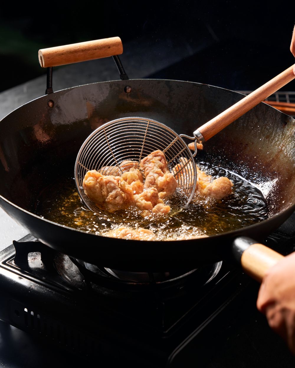 Crispy Korean fried chicken being cooked in a wok on a stovetop with oil and spider strainer