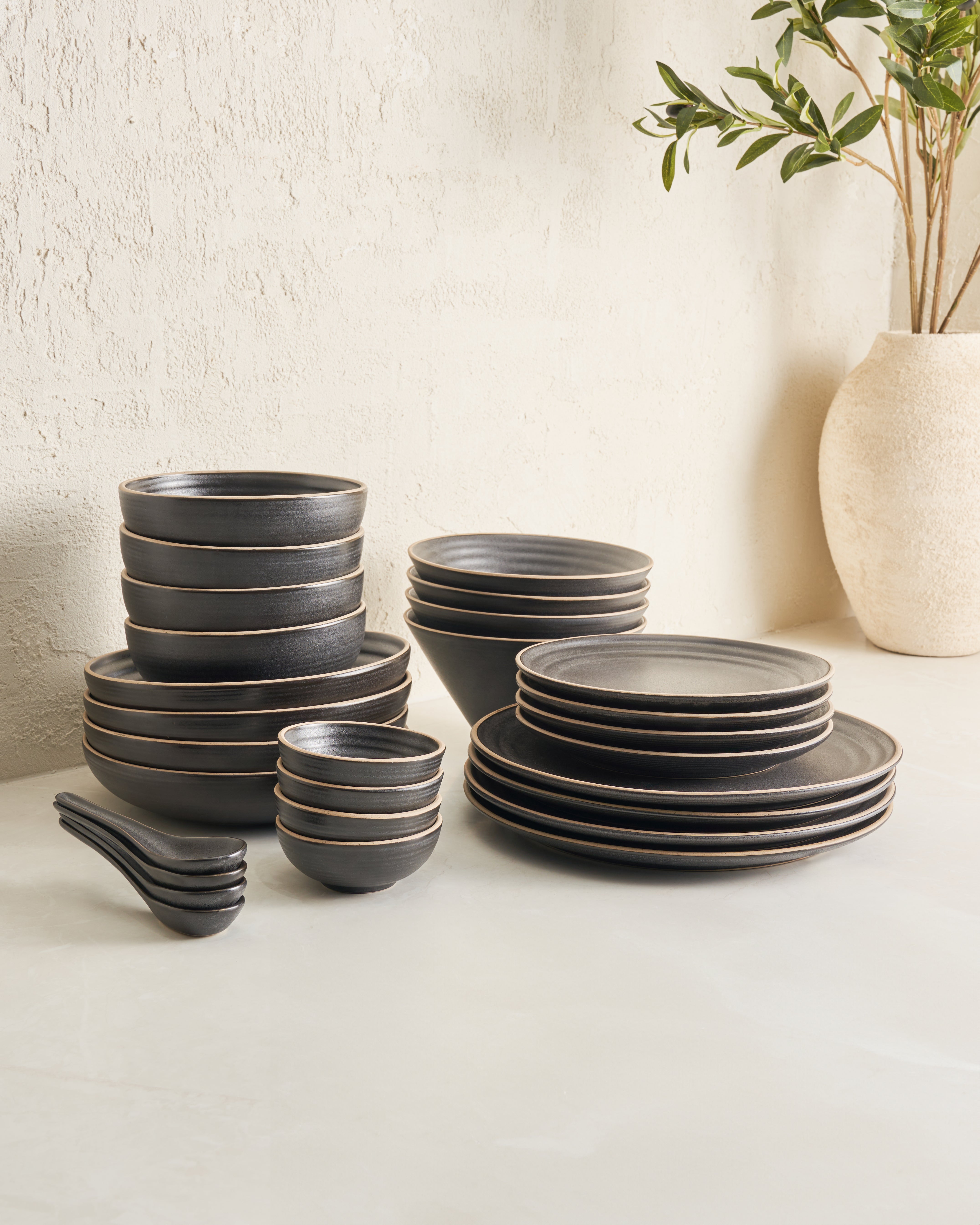 Charcoal stoneware dinnerware set with plates, bowls, and spoons on a light tabletop