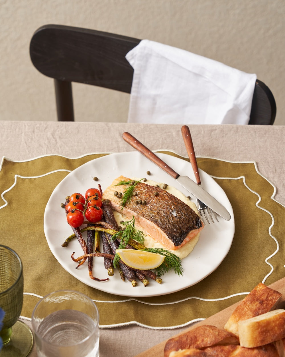 Seared salmon fillet with roasted carrots, tomatoes, lemon wedge and herbs on a ceramic plate