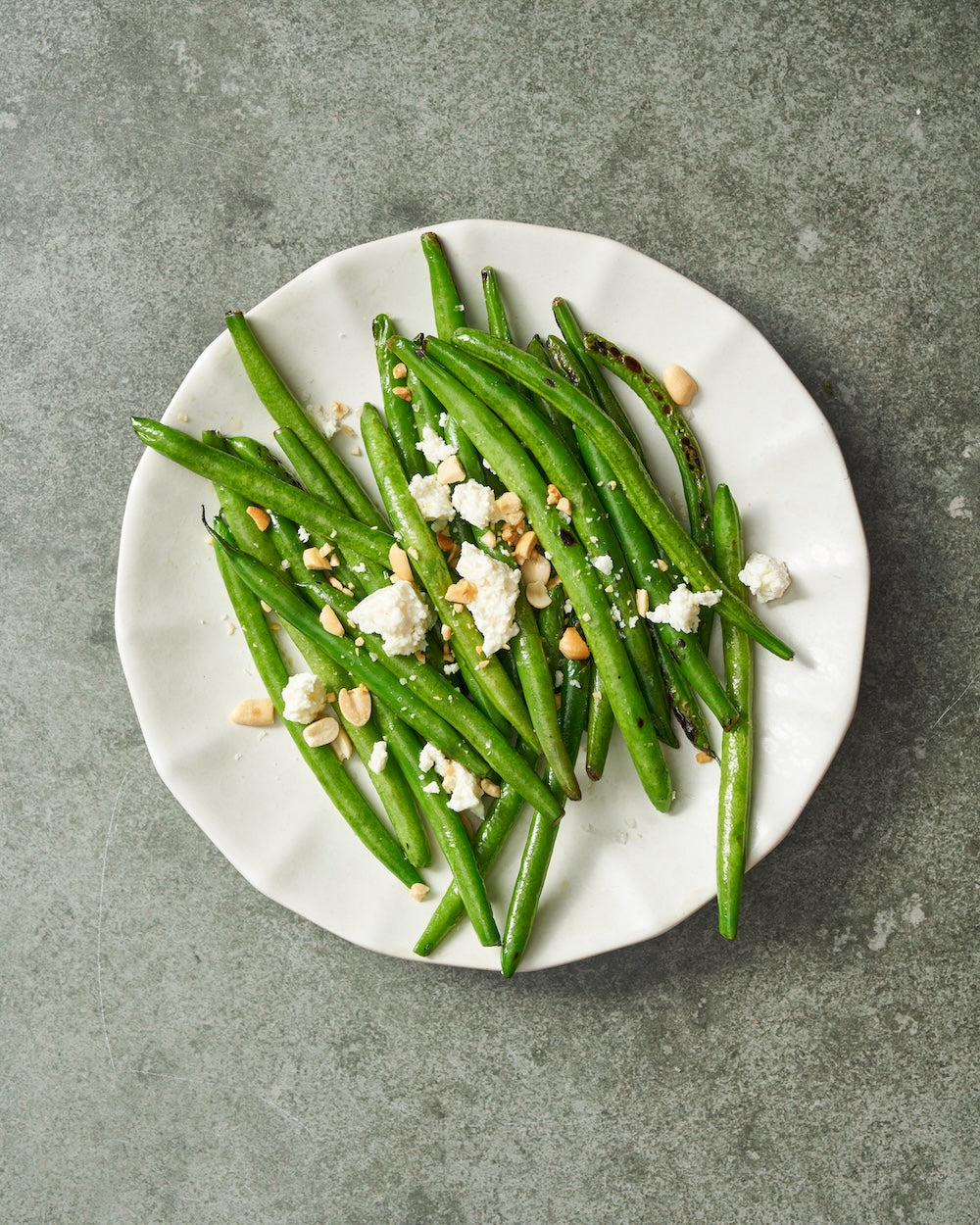 Grilled green beans with crumbled cheese and nuts on a white ceramic plate