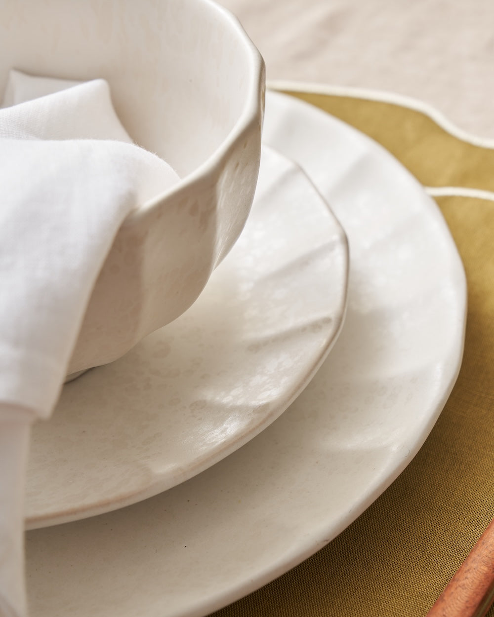 Textured white ceramic bowl and plates set on a beige tablecloth with a gold placemat