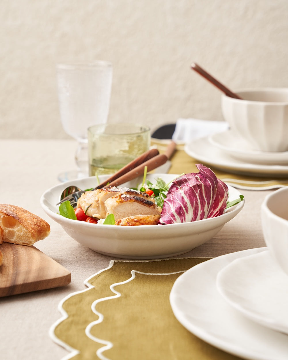 Ceramic dinnerware set with salad, bread, and glasses on an elegant dining table