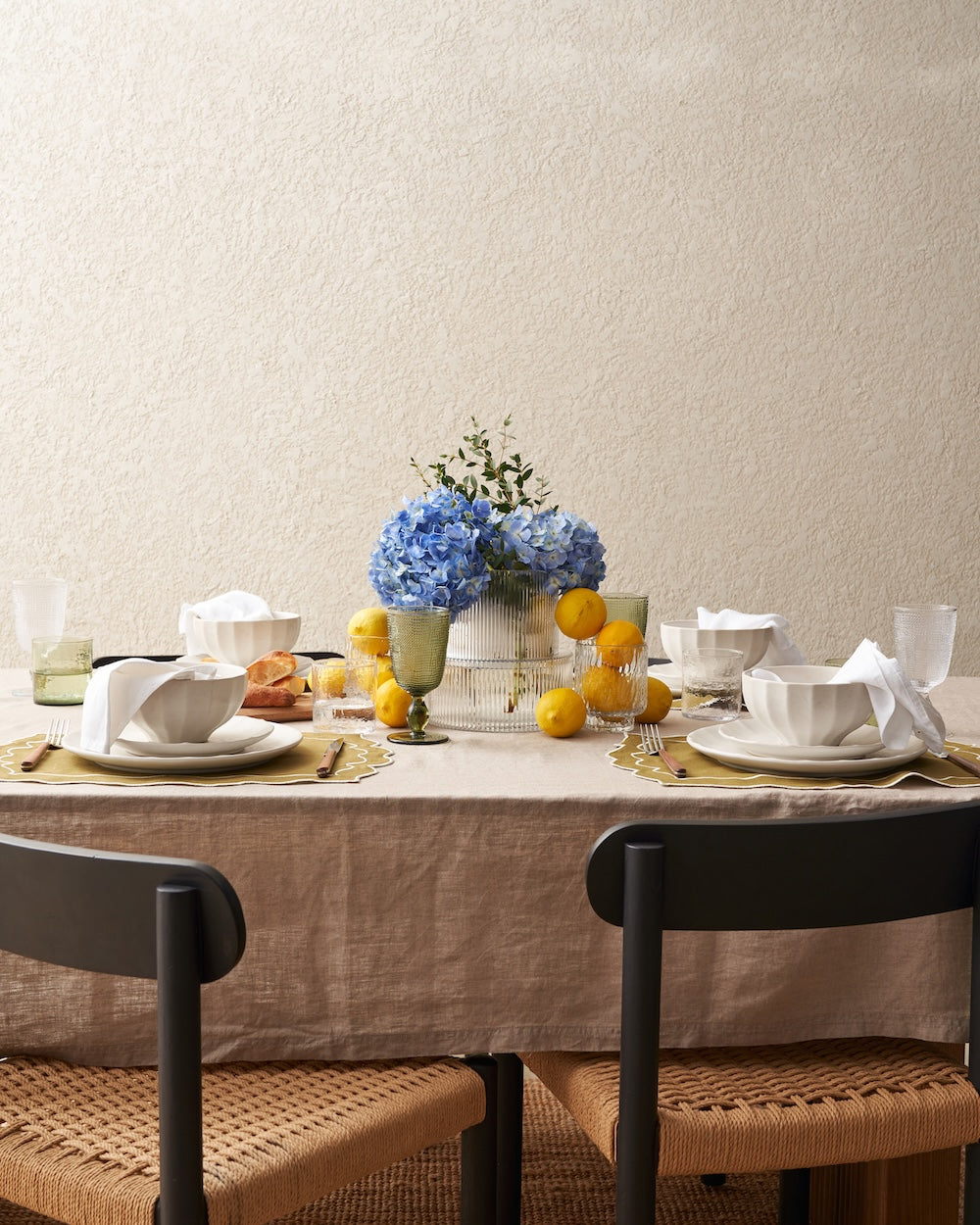 Elegant dining table with ceramic bowls, lemons, hydrangeas, and linen tablecloth