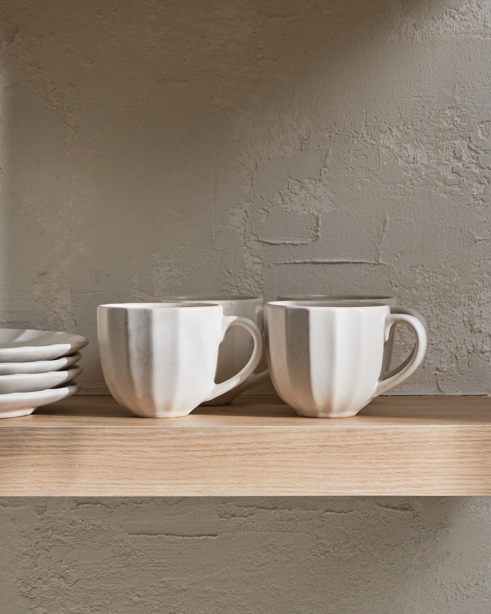 Two textured ceramic mugs and stacked plates on a wooden kitchen shelf