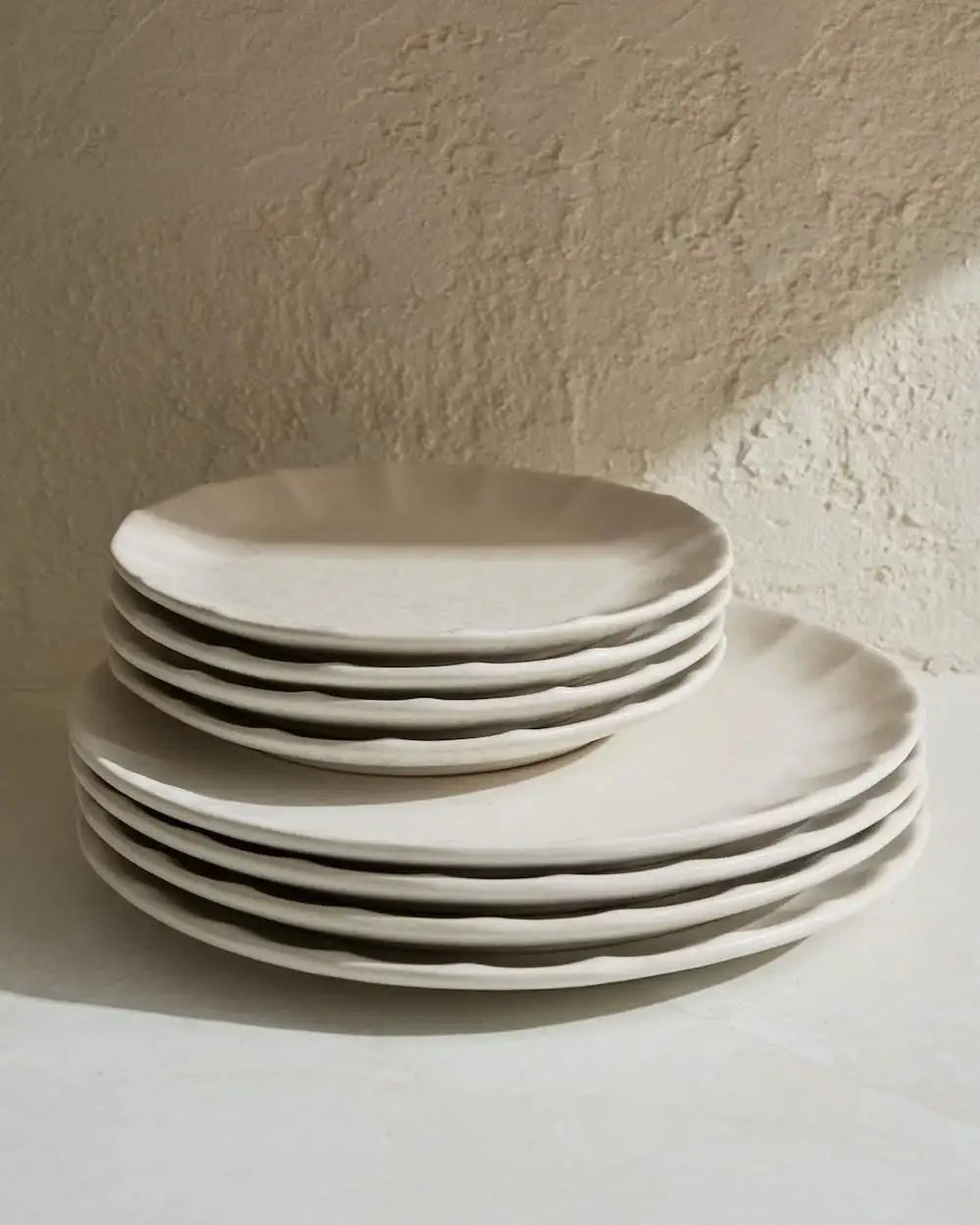 Stack of rustic cream ceramic plates with wavy edges in a textured kitchen setting