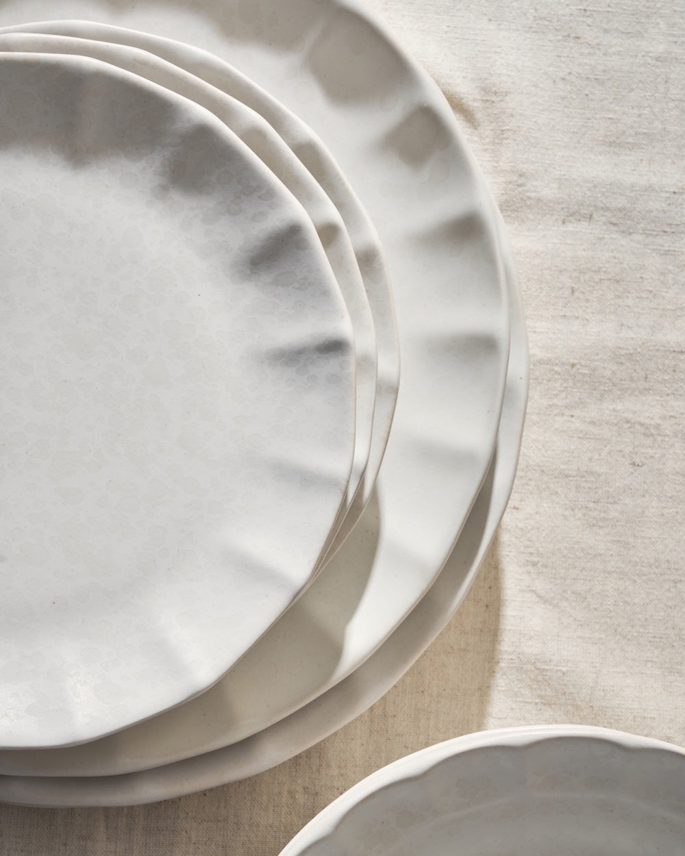 Stack of white ceramic plates with scalloped edges on a neutral tablecloth