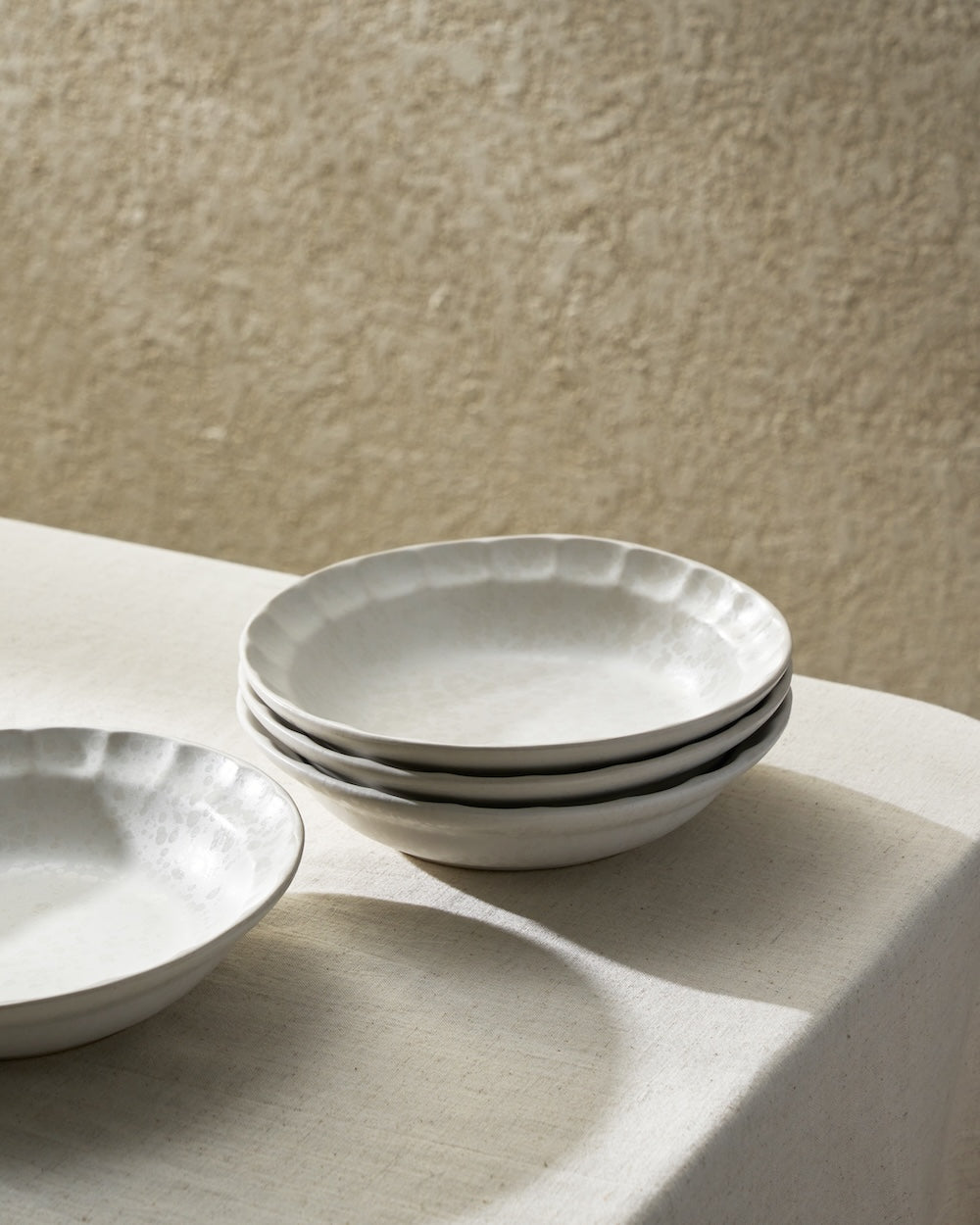 Stack of handcrafted white ceramic bowls on a neutral tablecloth under soft light
