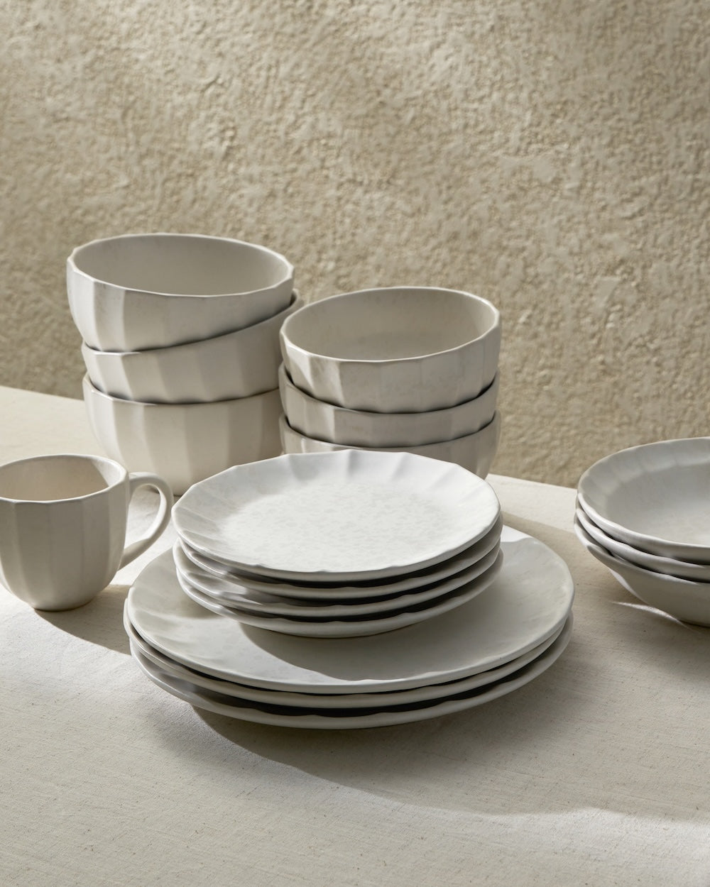 Stacked white ceramic plates, bowls, and a mug on a neutral tabletop in soft natural light