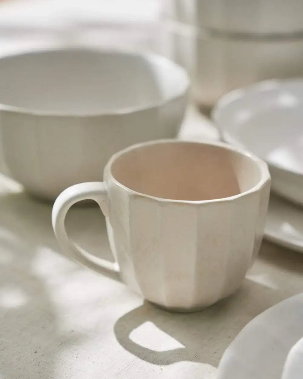 Asoke ceramic coffee mug with handle and matching white bowls and plates on light fabric backdrop
