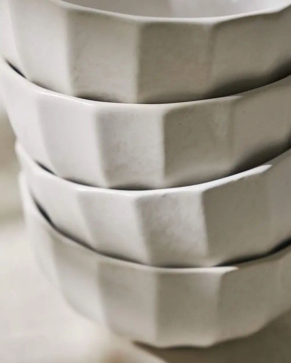 Close-up of stacked neutral-toned faceted ceramic bowls, minimalist kitchenware by Marion Grasby