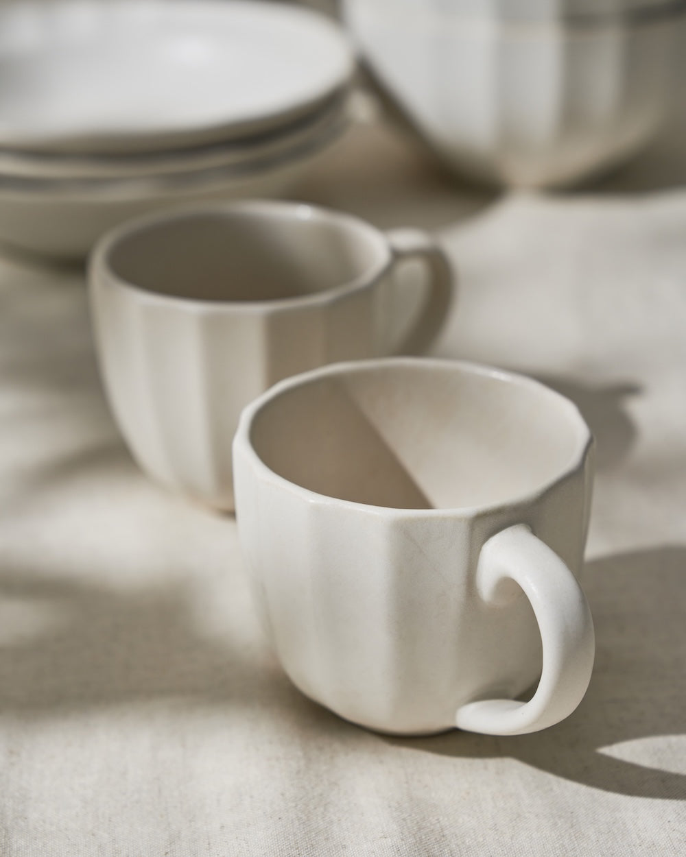 Two fluted ceramic mugs with stacked plates on a neutral tablecloth in soft natural light