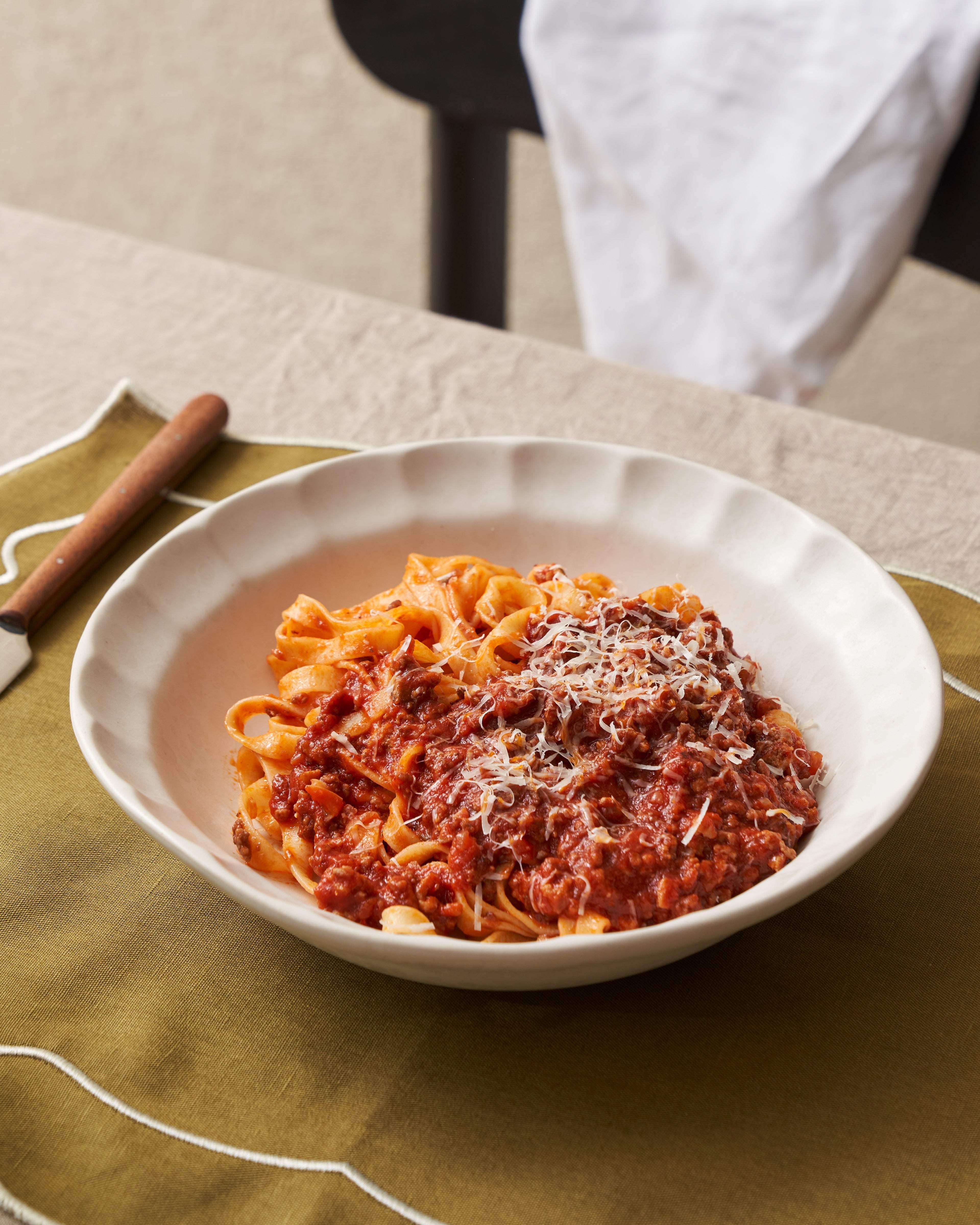 Ceramic pasta bowl with tagliatelle and tomato meat sauce, set on an olive napkin