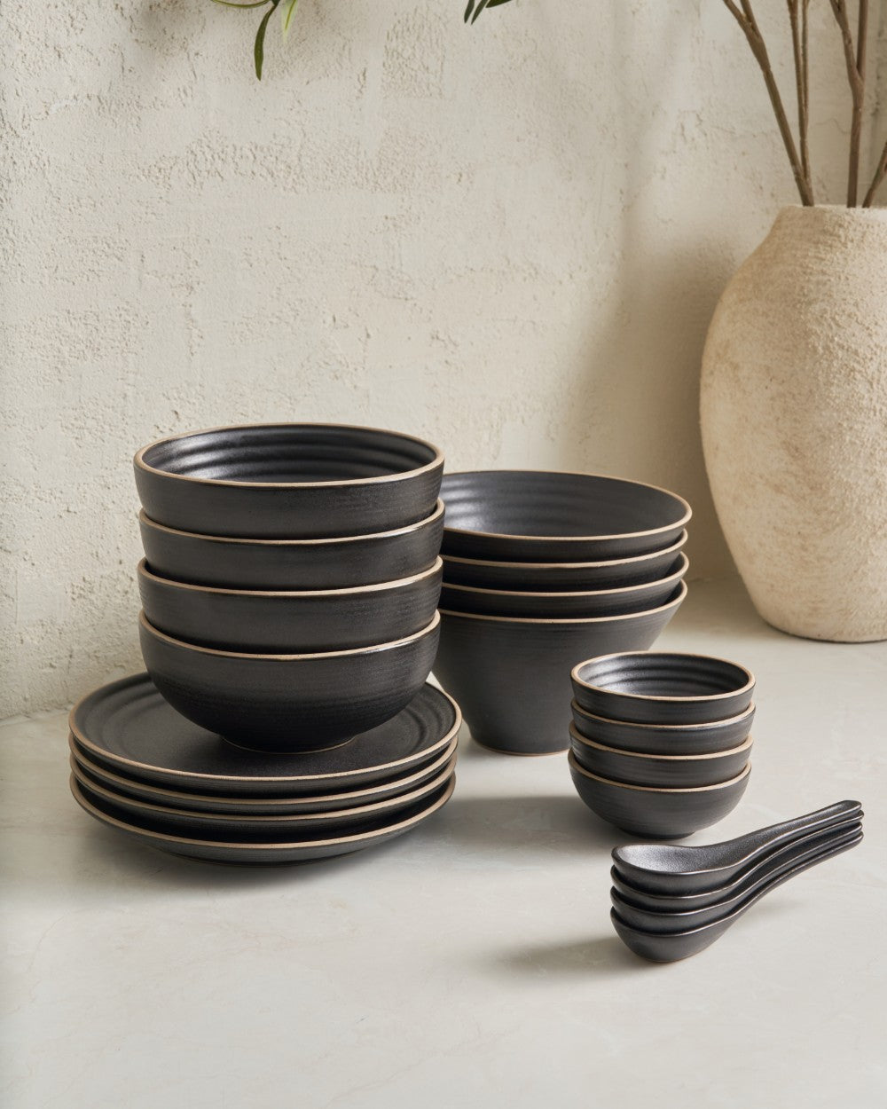 Charcoal ceramic dinnerware set with bowls, plates, and spoons on a light surface