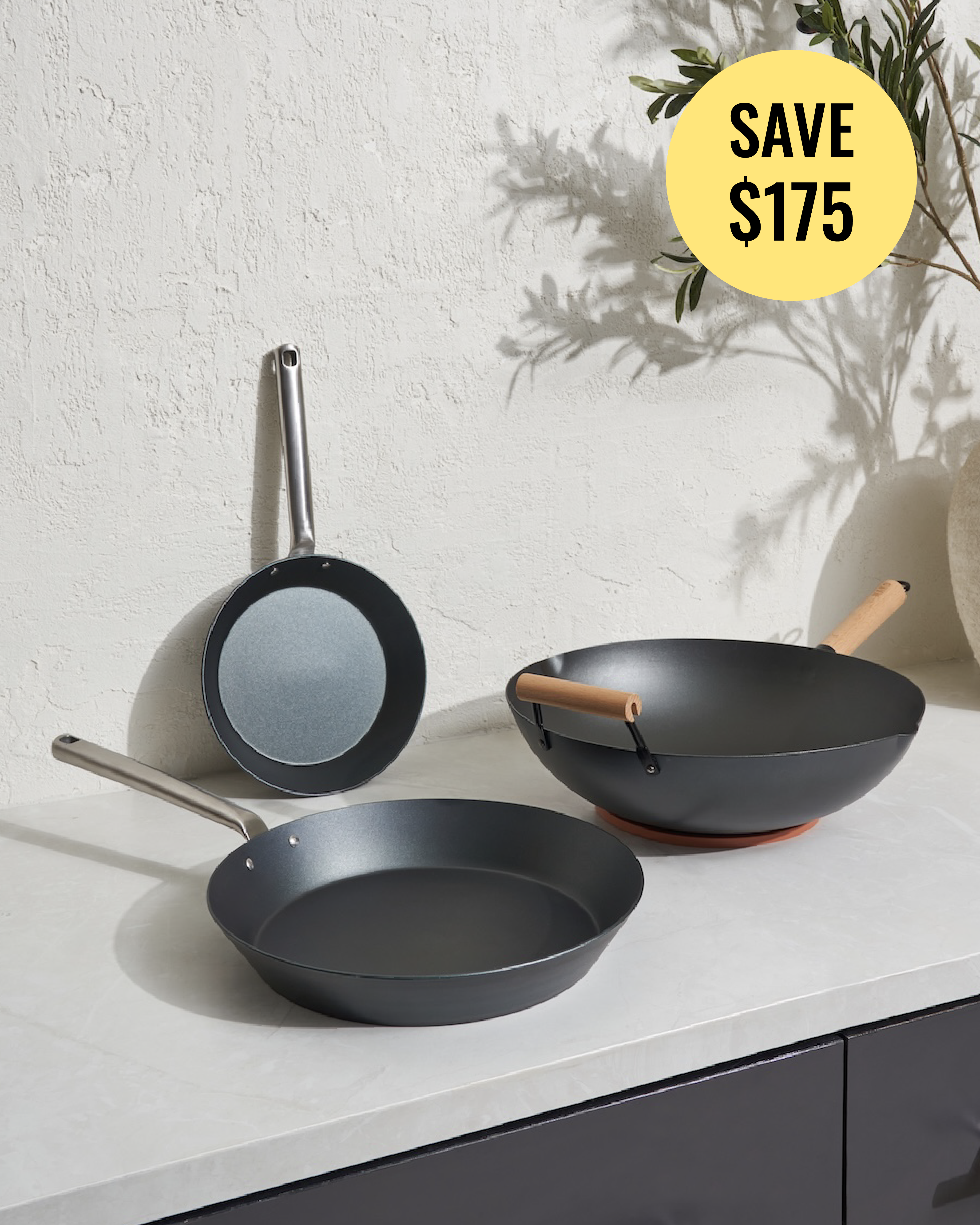 Three non-stick cookware pieces displayed on a white countertop against a textured white wall: a frying pan with a stainless steel handle, a deep pan with a silver handle, and a wok with a wooden handle. A yellow circular badge in the top right reads 'SAVE $175'.