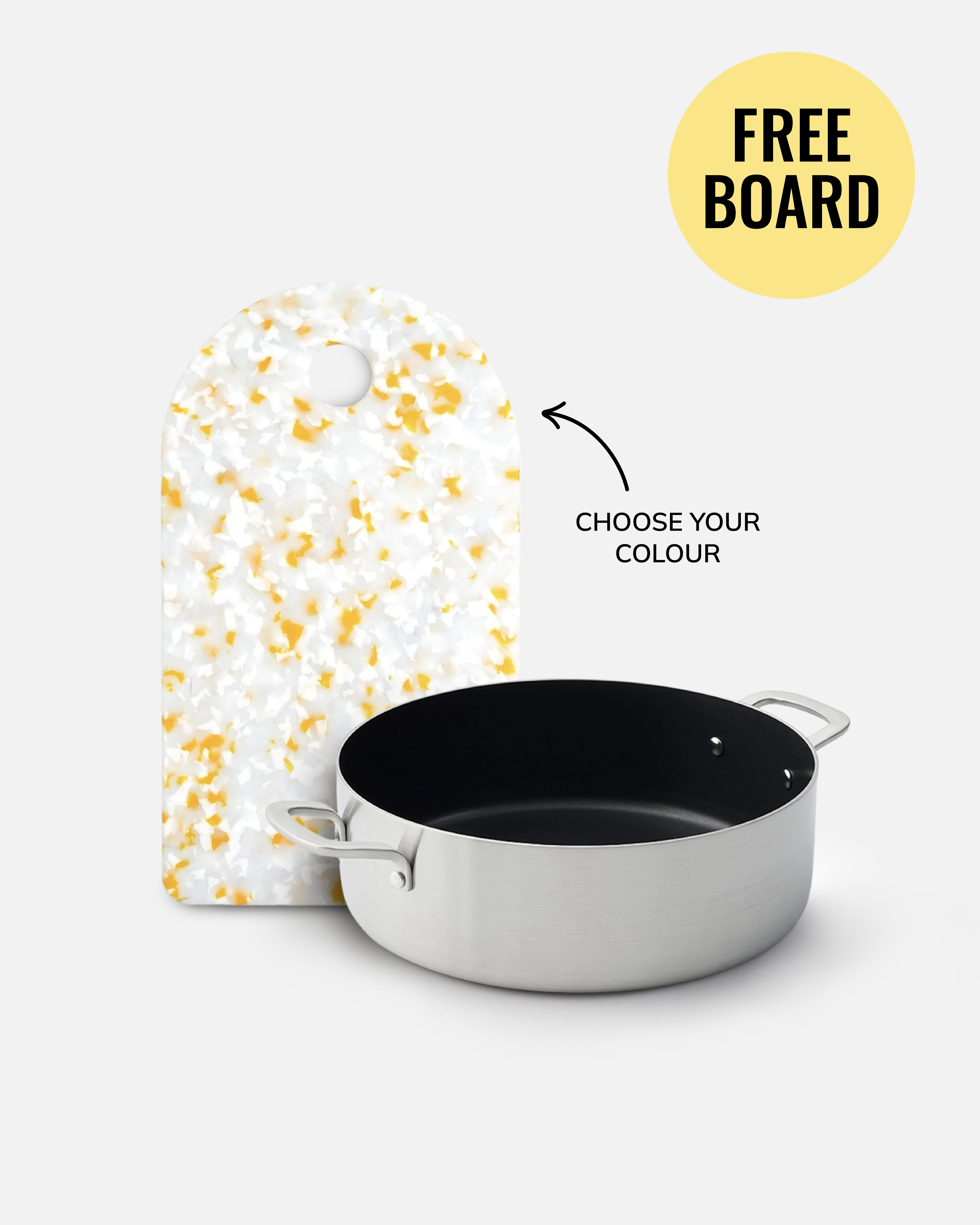 A stainless steel saucepan with a black interior is shown in front of a white cutting board with yellow speckles on a light gray background. A yellow circle reads 'FREE BOARD' with an arrow pointing to the cutting board and text reading 'CHOOSE YOUR COLOUR'.