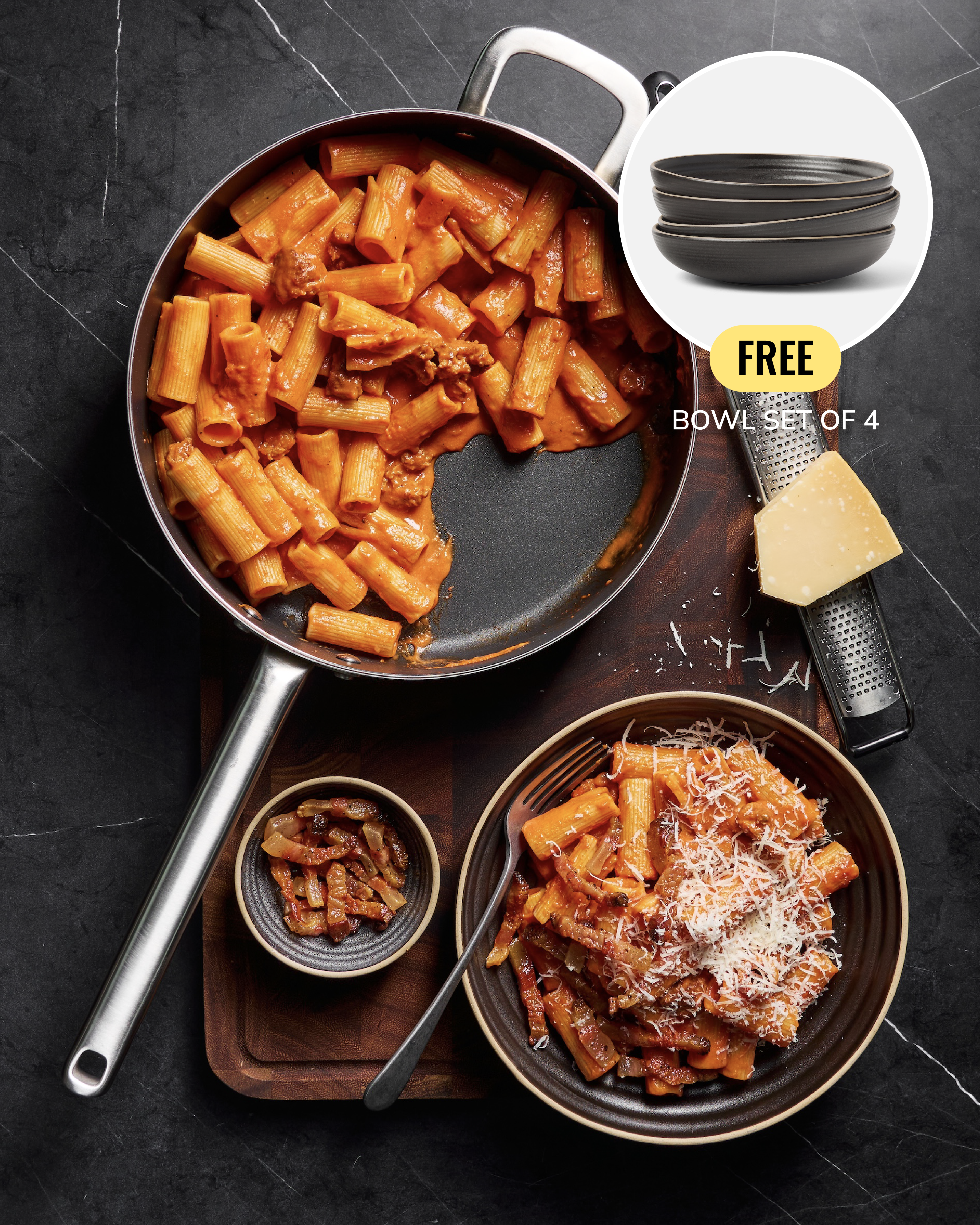 A styled kitchen scene showing a large skillet filled with pasta and meat, a plated serving of pasta with cheese, and a promotional inset of a free bowl set of 4. The cookware is photographed on a dark countertop with food props and a grater around them.
