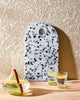 Speckled white and black terrazzo cutting board with clear carafe and glasses of water with lemon