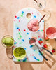 Colorful cutting board with strawberry and matcha ice cream, ice cream scoop, and strawberries