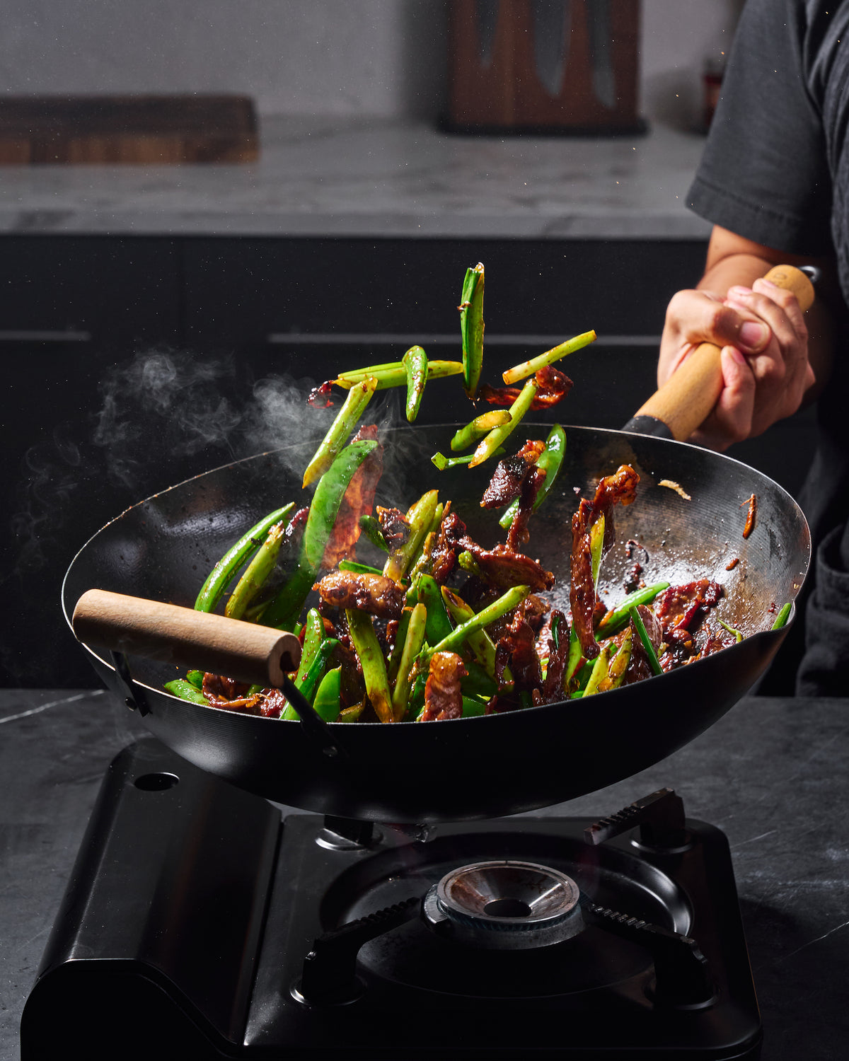 Beef, asparagus and snow pea stir-fry being tossed in a MAKO black steel wok over a gas burner.