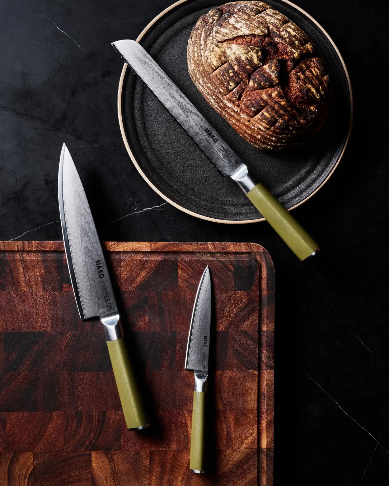 MAKO Japanese Steel Knife Trio - Olive Green in use with loaf od bread wooden chopping board on dark marble benchtop