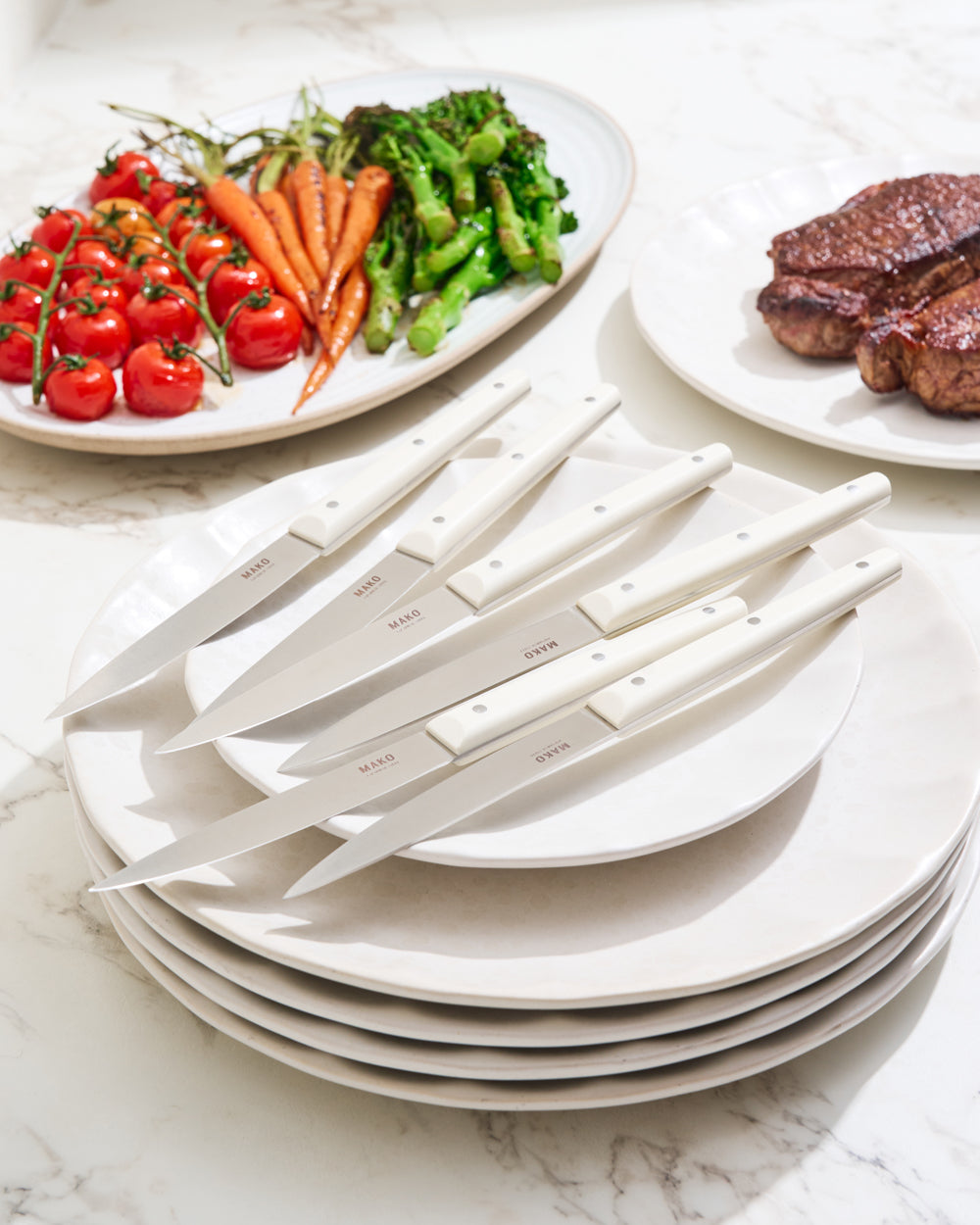 MAKO Steak Knife Set of 6 - Cream lifestyle table setting on white Calida plates. Vegetables and steak in background