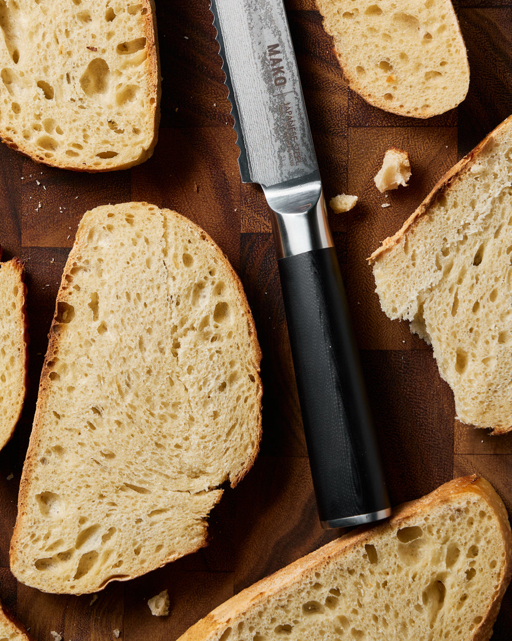 MAKO Japanese Steel Black 8″ Bread Knife close up on wooden chopping board of handle with bread slices