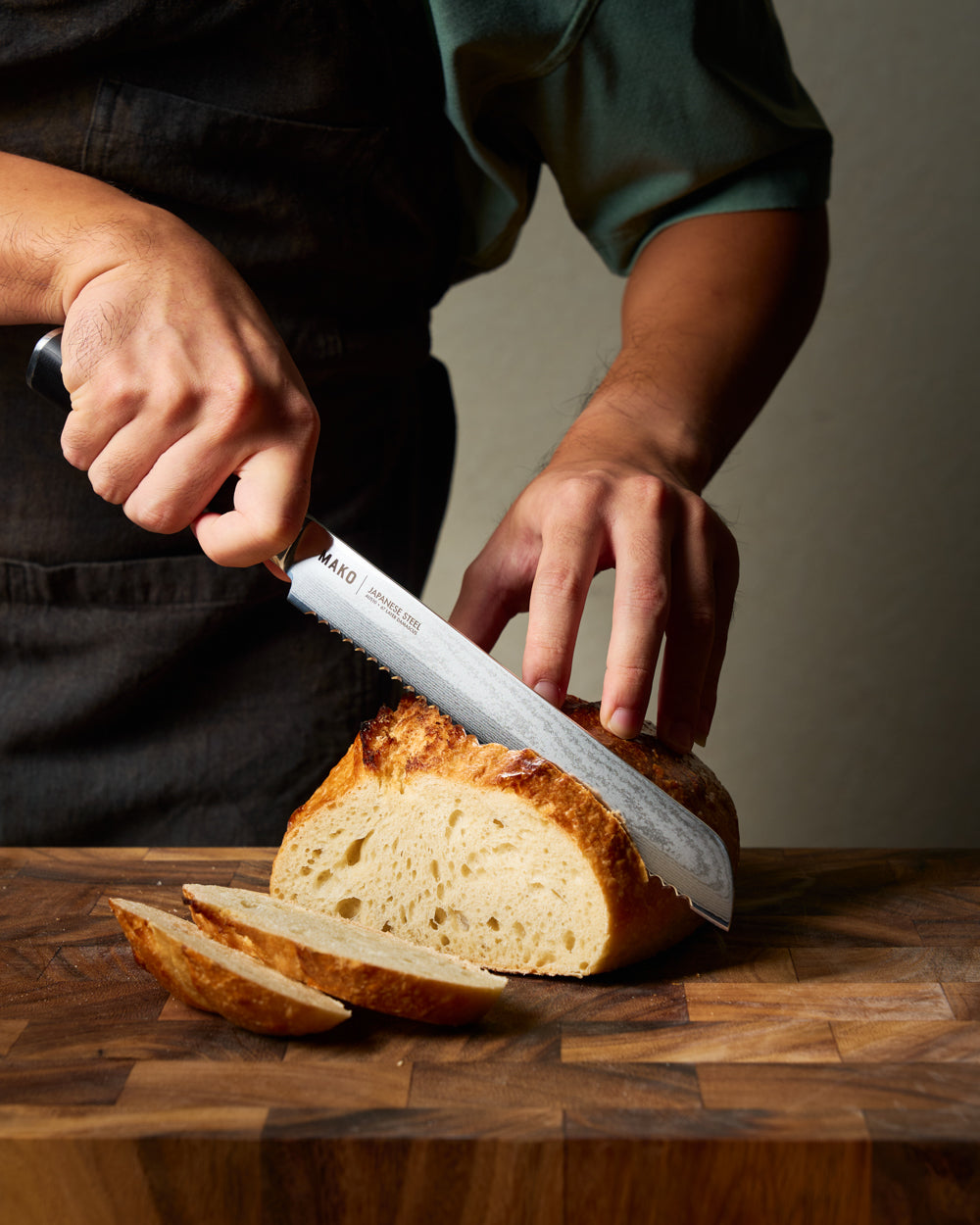 MAKO Japanese Steel Black 8″ Bread Knife in use on wooden chopping board cutting bread CookDineHost