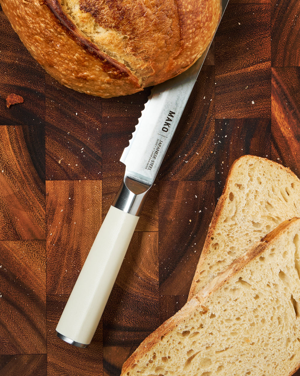 MAKO Japanese Steel Cream 8″ Bread Knife CookDineHost close up on wooden chopping board with load and slices of bread