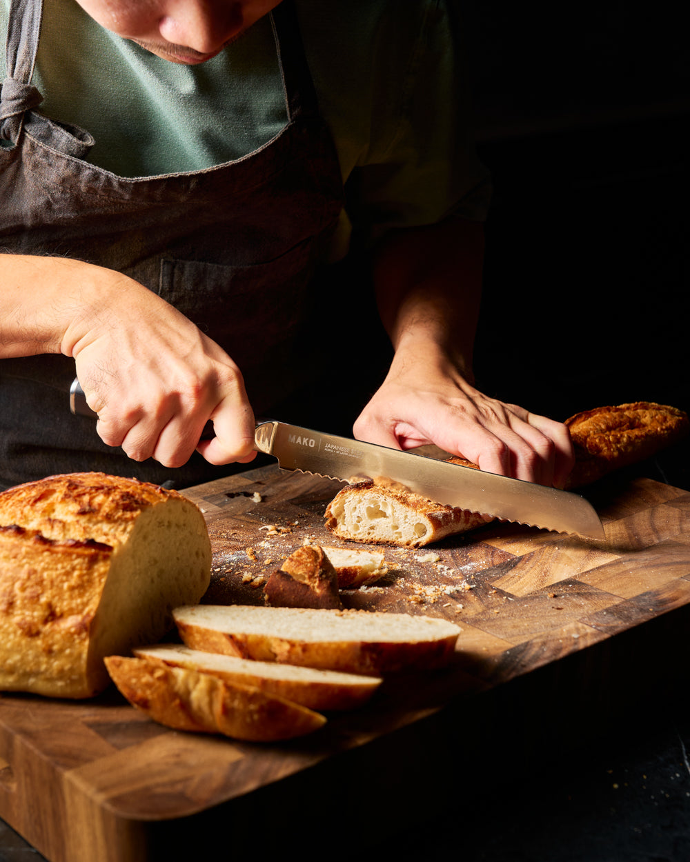 MAKO Japanese Steel Black 8″ Bread Knife in use cutting baguette on wooden chopping board CookDineHost