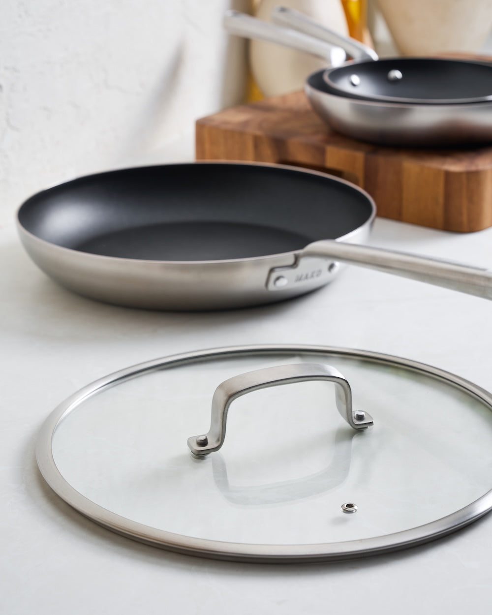 Stainless steel non-stick frying pan with glass lid on a modern kitchen counter