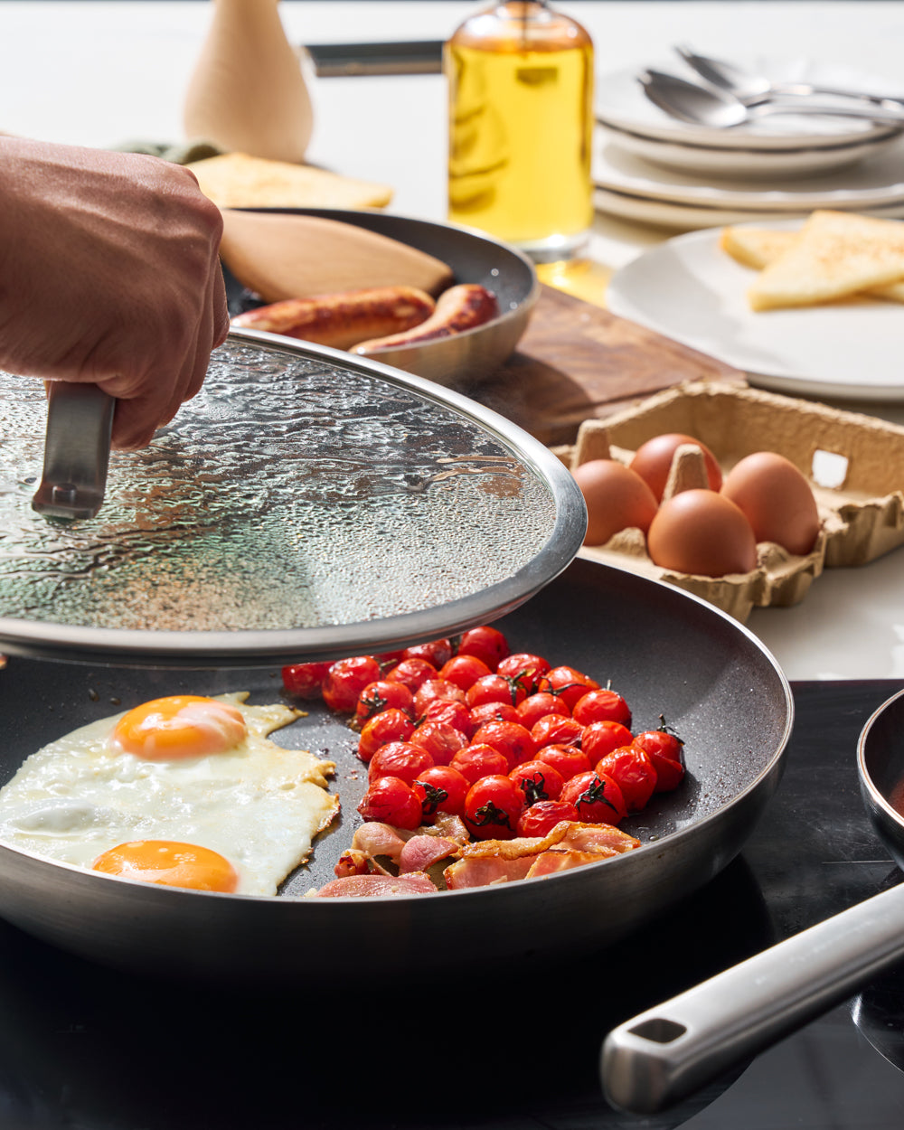 Non-stick frying pan with eggs, blistered tomatoes, and bacon on a kitchen stovetop