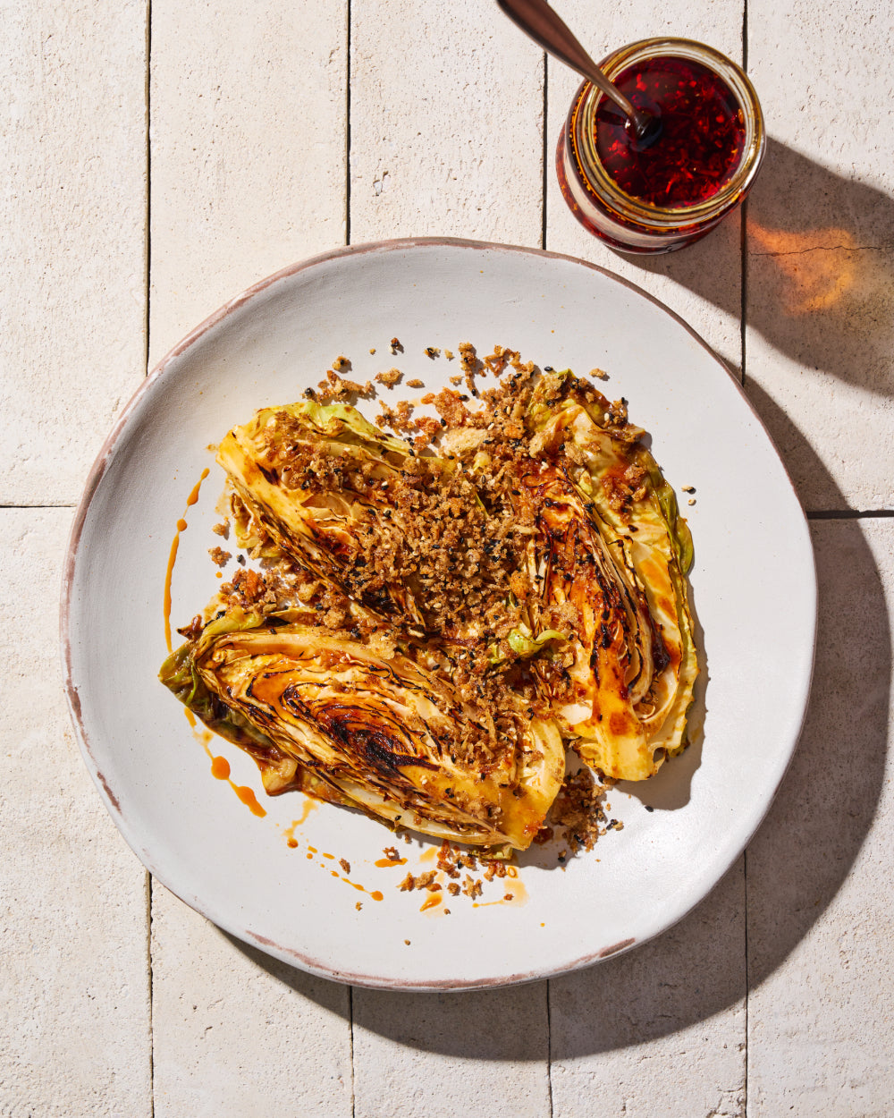 Charred gochujang butter cabbage wedges topped with golden crunchy breadcrumbs and a drizzle of chilli oil, served on a plate