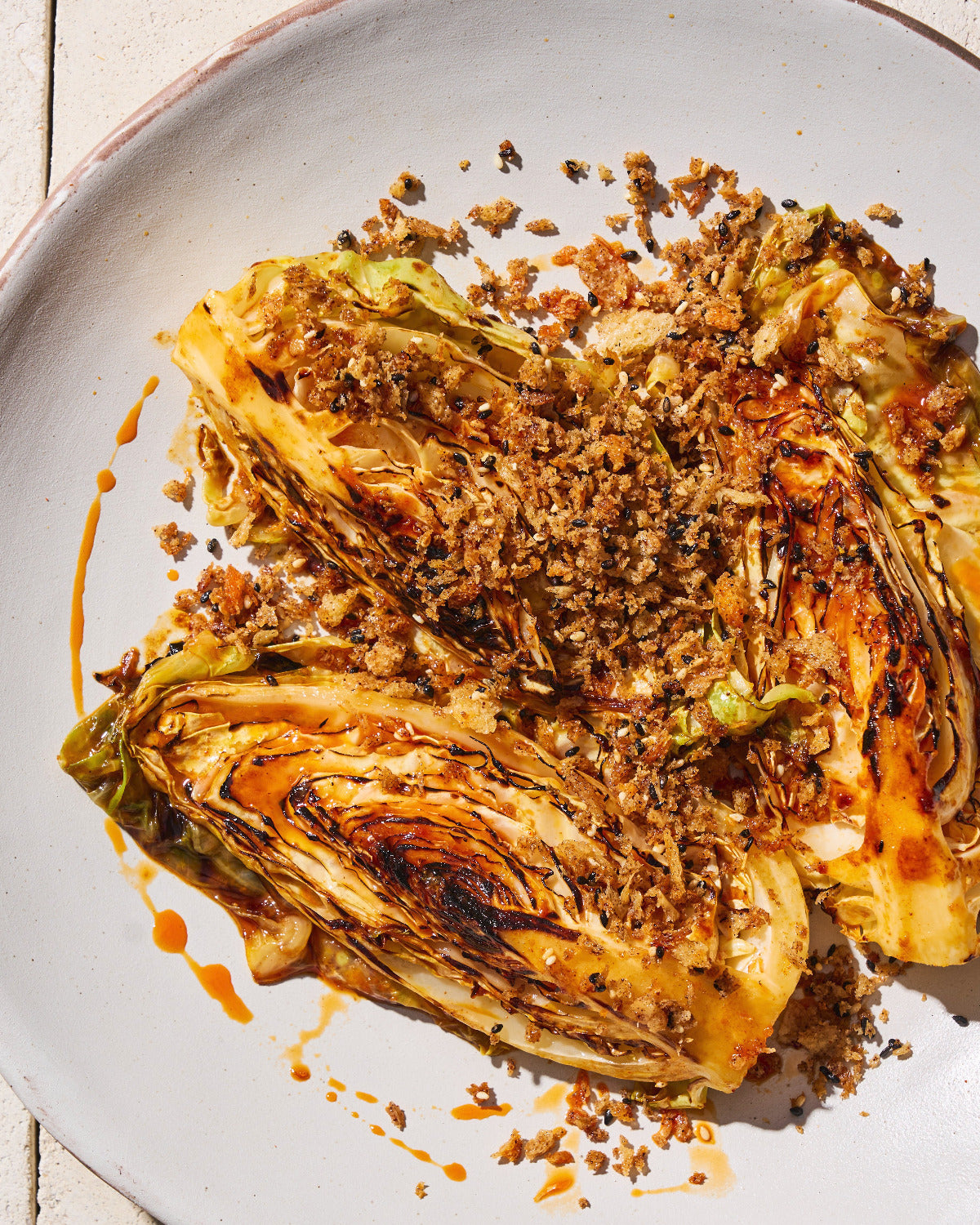 Charred gochujang butter cabbage wedges topped with golden crunchy breadcrumbs and a drizzle of chilli oil, served on a plate